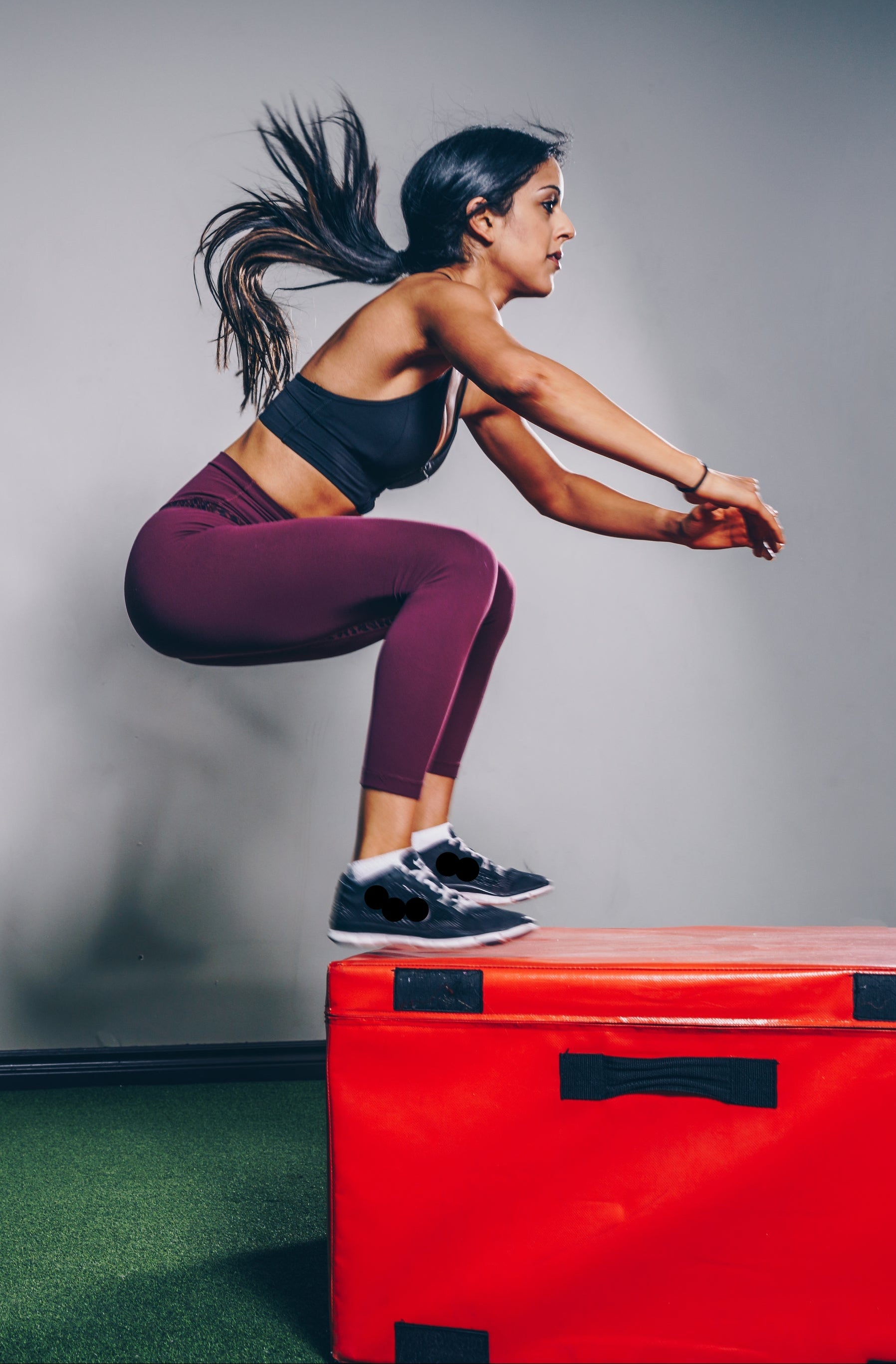 Woman performing box jumps on a red box against a gray wall.